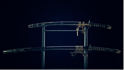 A set of ancient samurai swords from Japan stand on display in the dark.