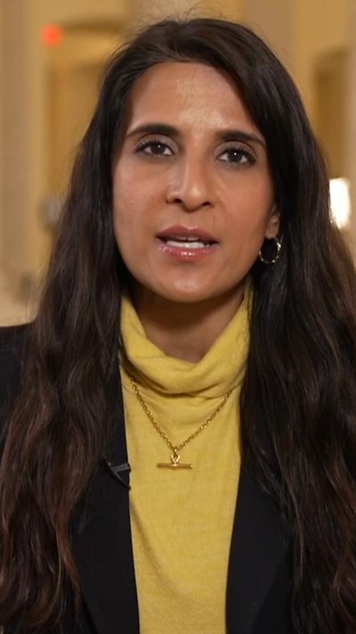 Woman wearing a yellow turtle neck top and black blazer speaks to the camera inside Congress.