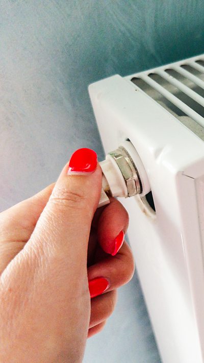 A close-up on a hand with red finger nails holding a radiator valve