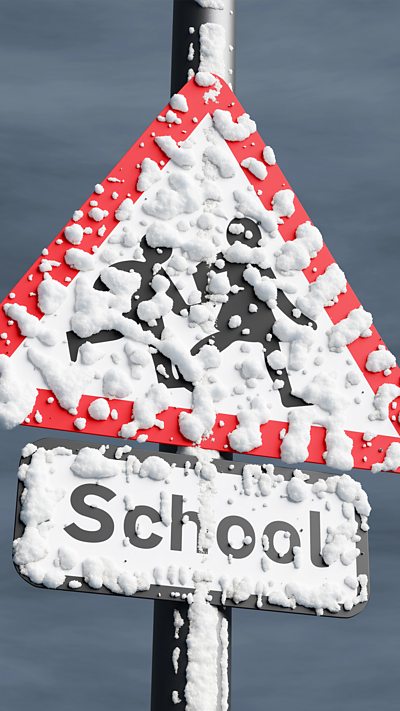 A school road sign on a pole covered in snow with a dark grey sky behind