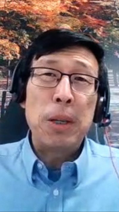 A man wearing headphone and glasses in a blue shirt with a forest background