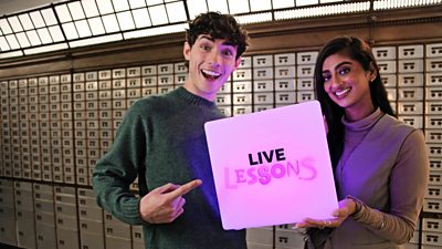 Joel and Harleen from Live Lessons stood smiling, holding a light up cube in a pinky colour that has Live Lessons branding on it Joel is pointing at the words.