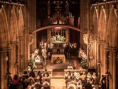The interior of a beautiful church, adorned with Christmas lights, flowers and candles, with a choir at the head of the church.