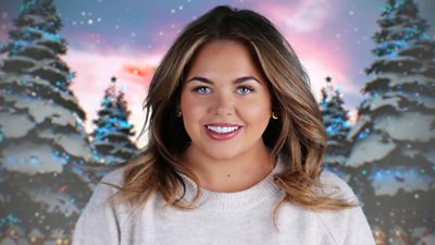 A woman in a light jumper smiles to camera, set against a backdrop of snowy Christmas trees