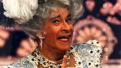 Photo from Being Stanley Baxter, featuring the television star wearing elegant earrings, an elaborate hair piece, and colourful clothing. 