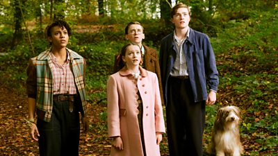 Four children and a dog stand in a forest looking up at something in the sky above them