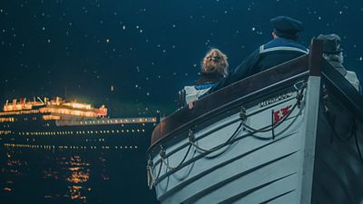 Three figures sit in a lifeboat facing a large cruise liner, still lit as it floats on the sea at night