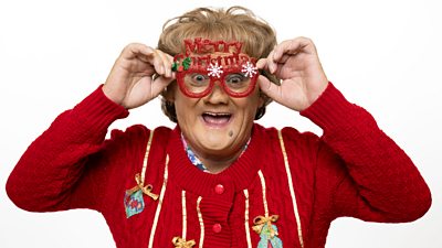 A character in a red festive cardigan smiles to camera, wearing red novelty glasses that read Merry Christmas