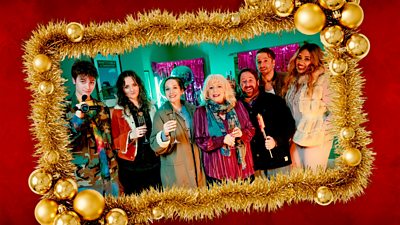 A portrait of a family all raising a toast is set in a gold tinsel frame, with one young man at the end holding a camcorder filming them