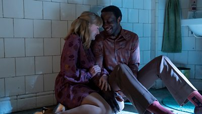 A man and a woman sat on a bathroom floor giggling in each other's arms with their heads pressed together