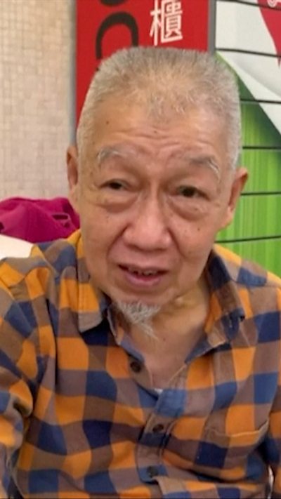 Older man in chequered shirt speaks to camera