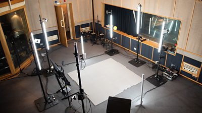 A recording studio with a patch of floor panelling laid out to highlight the performance space, surrounded by bright lighting and capture cameras on every side.