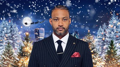 A man in a suit (JB Gill) looks to camera with a festive backdrop.