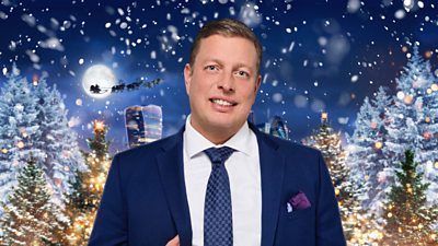 A man in a suit poses outside a festive, snowy backdrop