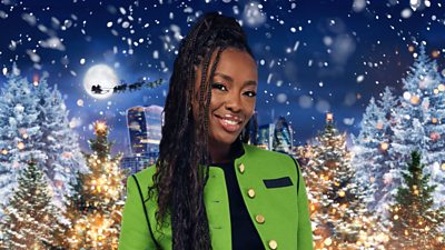 A woman with braids and a green jacket smiles with a Christmas background