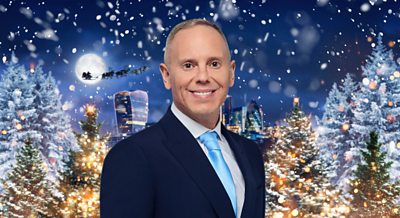 A man in a dark blue suit smiles in front of a Christmas scene