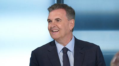 A man in a suit smiles and laughs in a boardroom