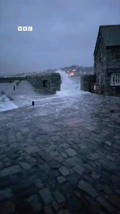 St Michael's Mount in Cornwall. White foam from the sea. Grey clouds. BBC logo in top left corner,