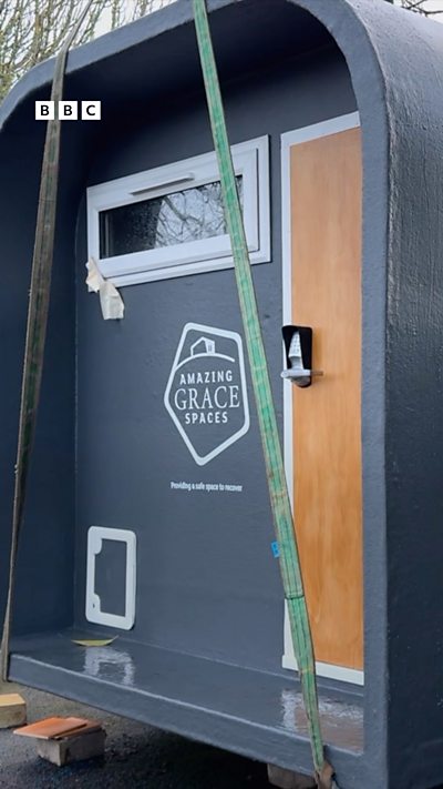 The front door of a sleep pod. The pod is grey, the door is brown.