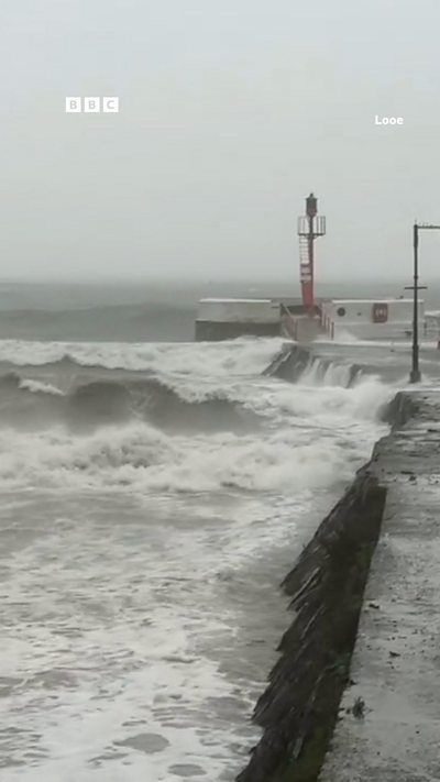 A wall with grey sea and white sea foam. The sky is grey.