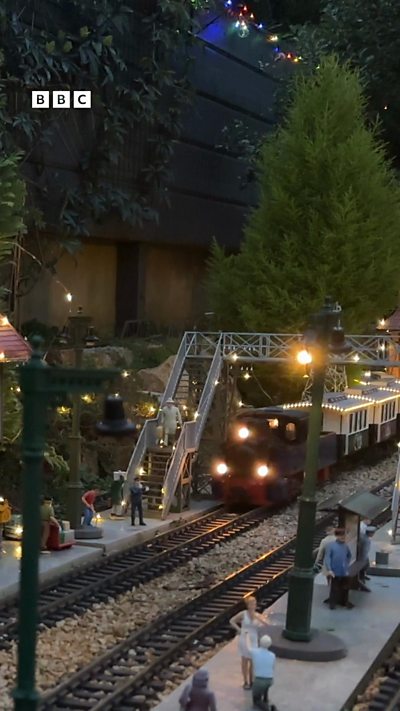A miniature train on a garden track surrounded by fairy lights