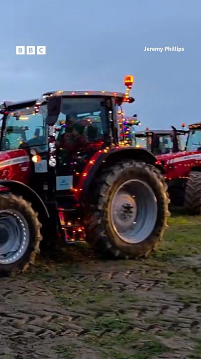 A red tractor covered in fairy lights stands in a field