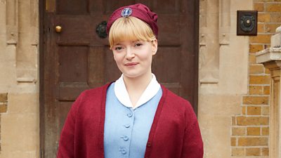 Natalie Quarry in character as Nurse Rosalind Clifford. Wearing a midwife uniform, she stands on the steps to Nonnatus House.