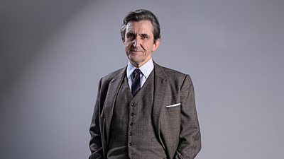 Stephen McGann in character as Dr Turner. Wearing a grey three-piece suit. 