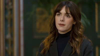 Close-up image of a woman wearing a grey blazer over a black jumper. 