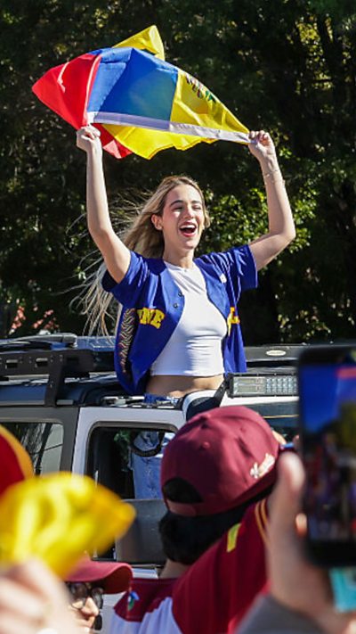A woman waving a Venezuelan flag with her upper body sticking out on a car.