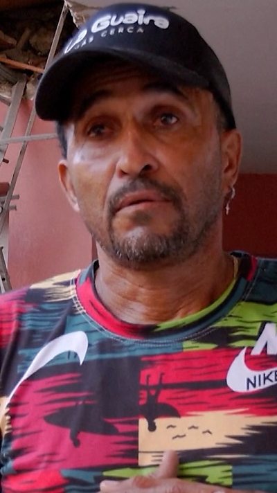 A man wearing a multi-coloured t-shit and a black cap.