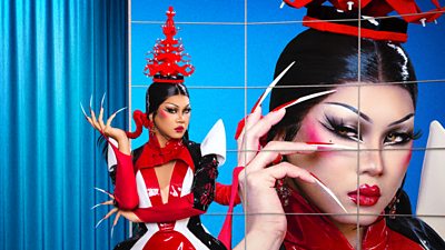 A drag queen (Gawdland) poses in an elaborate red headdress and hyper-long false nails 