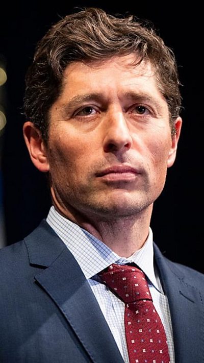 Man wearing a blue suit and red dotted tie looks off camera with a black background behind.
