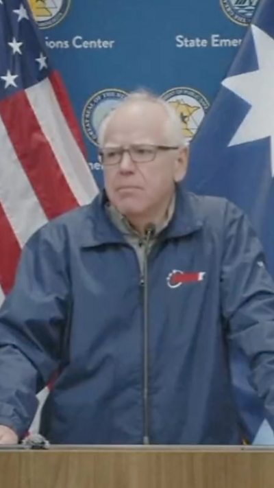 Tim walz is talking to the press in front of a podium.