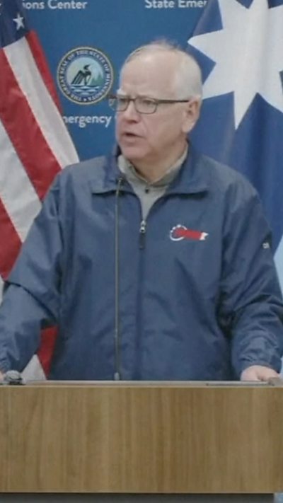 Tim Walz is talking to reporters in front of a podium.