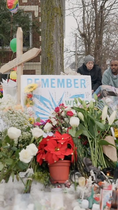 A sign saying "Remember" lays against a tree and behind flowers.