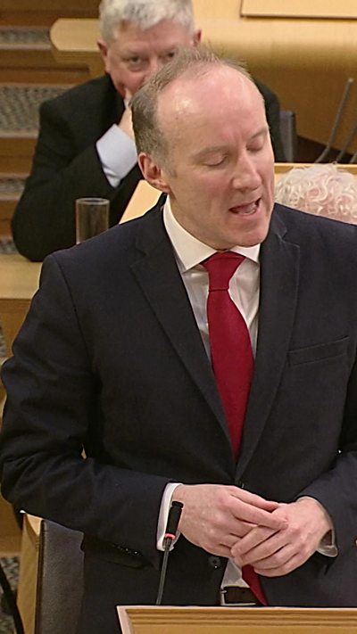 Balding man with dark suit and red tie.