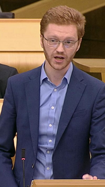 Red headed man in blue suit and purple shirt.