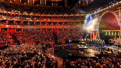 A large audience sits in a grand building before a stage. In a photo from a previous Olivier Awards, host Hannah Waddingham presents on stage before an audience in the Royal Albert Hall. 