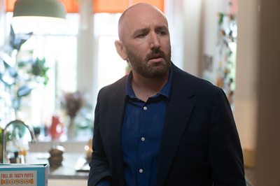 A man (David Carlyle who plays Bo in Dinosaur) stands looking concerned in a living room