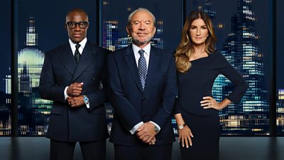 A man (Tim Campbell CBE) another man (Lord Sugar) and a woman (Baroness Brady CBE) pose outside a city skyline in navy blue formal dress 
