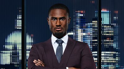 A man (Marcus Donkoh) looks determined with folded arms in a plum suit, as he stands outside a city landscape at night 