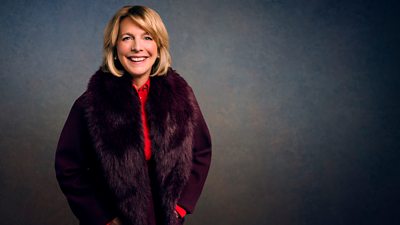 A woman in a deep burgundy coat and red shirt smiles to camera