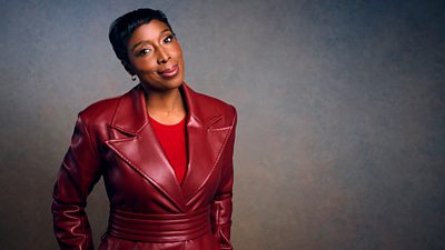 A woman in a deep red leather style coat smiles to camera