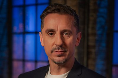 A man (Gary Neville) stands in a moody looking room.
