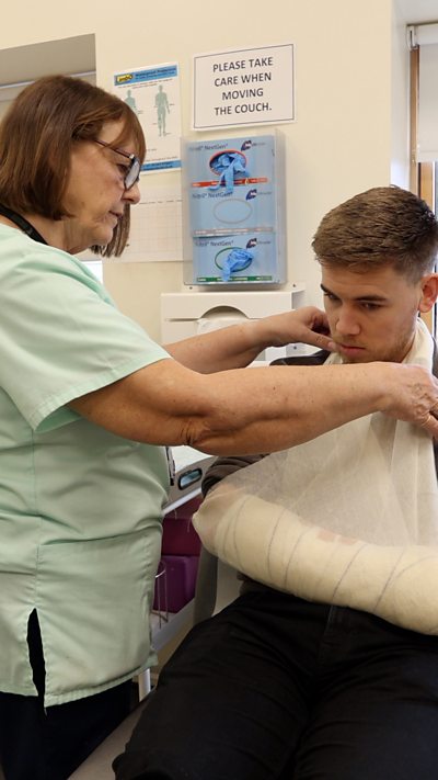 A man with his arm in a sling being seen to by a nurse