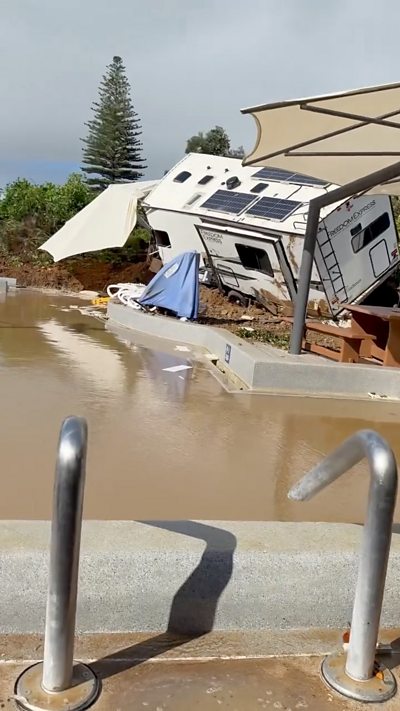 The aftermath of a landslide in New Zealand with a caravan on its side and a pool filled with murky brown water