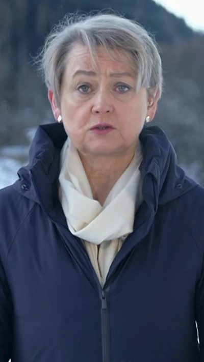 Yvette Cooper stands in front of a mountain wearing a white scarf and blue coat.