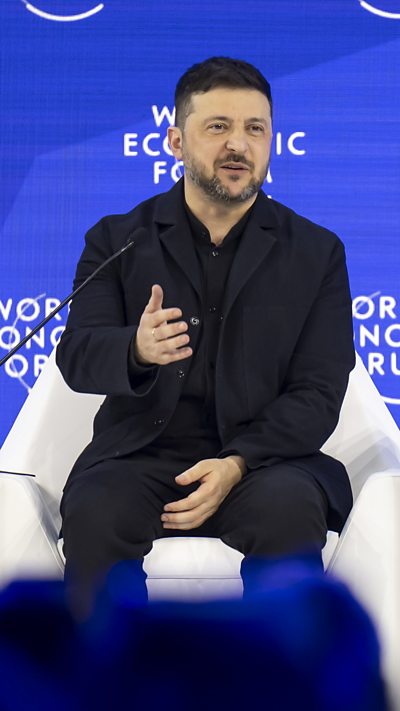 Ukrainian President Volodymyr Zelensky sitting on white chair on Davos summit stage