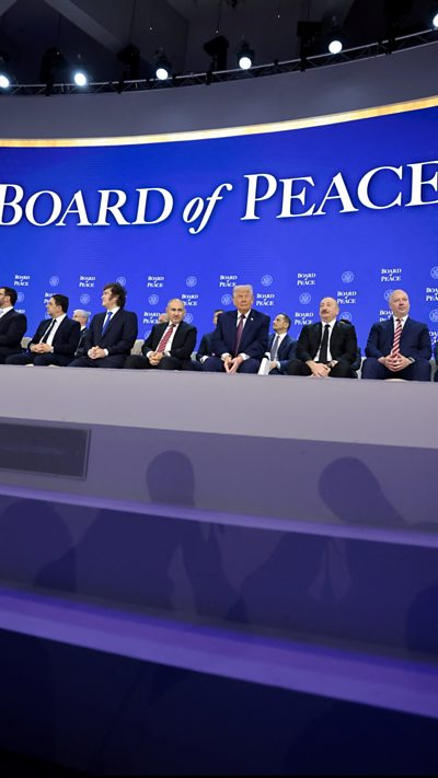 US President Donald Trump sitting with world leaders, sign reads 'Board of Peace'